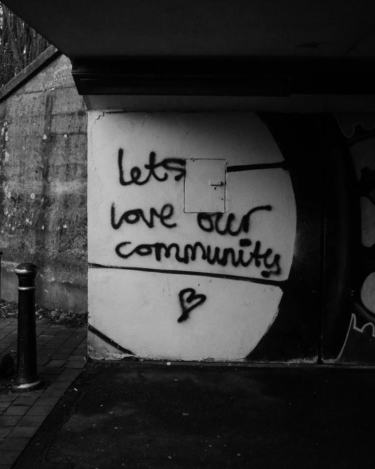 Black and white graffiti on a wall reads let's love our community with a small heart underneath.